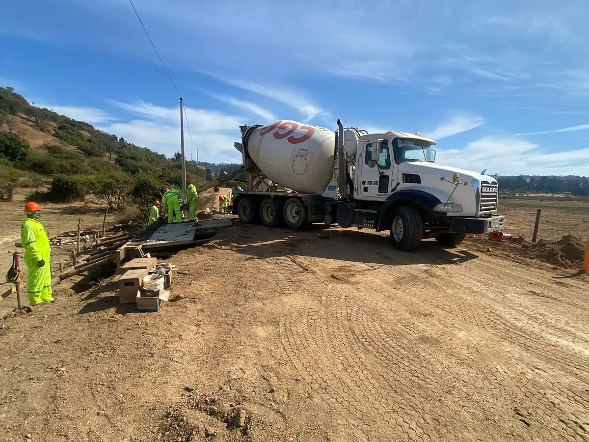 Camión mixer de hormigón junto a una cuadrilla trabajando en la obra de un camino rural